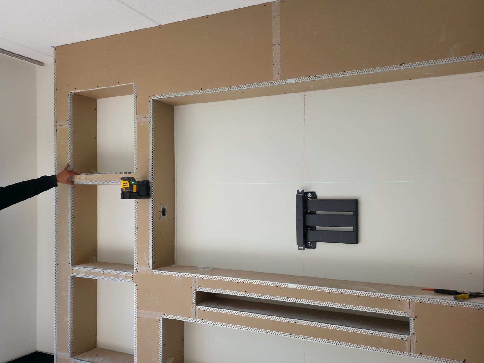 Cinewall bouwen: frame met gipsplaten en uitgespaarde nissen voor tv, haard en verlichting, met de tv beugel al op de wand gemonteerd