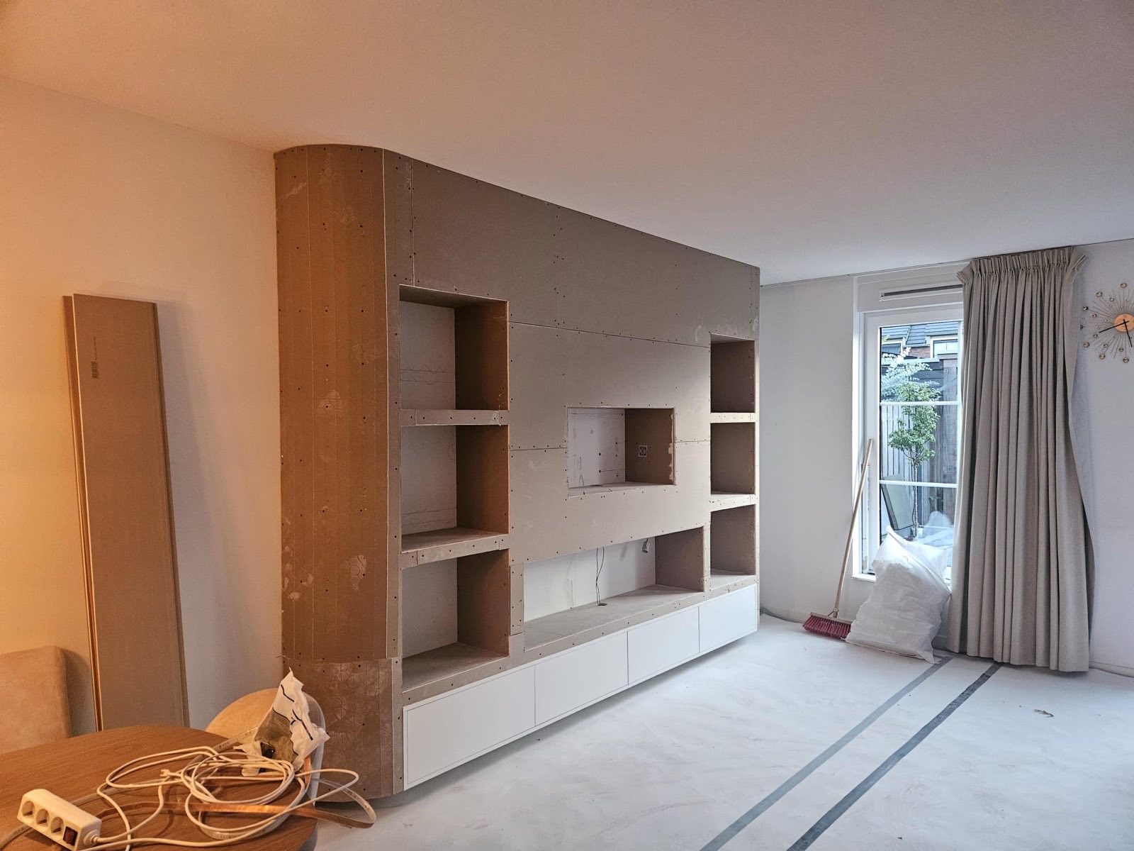 Cinewall in aanbouw: gipsplaten wand met open nissen, een uitsparing voor de tv en witte onderkasten, klaar om te stucen