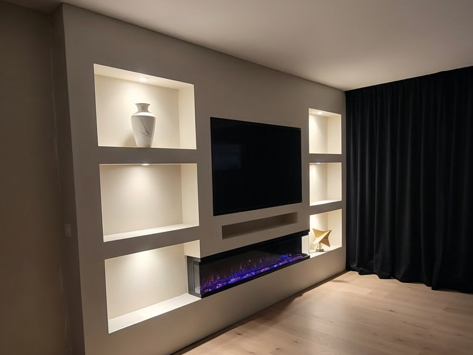 Cinewall op maat met zes verlichte nissen, dikke planken, verzonken tv en een brede elektrische haard in een gestucte tv wand