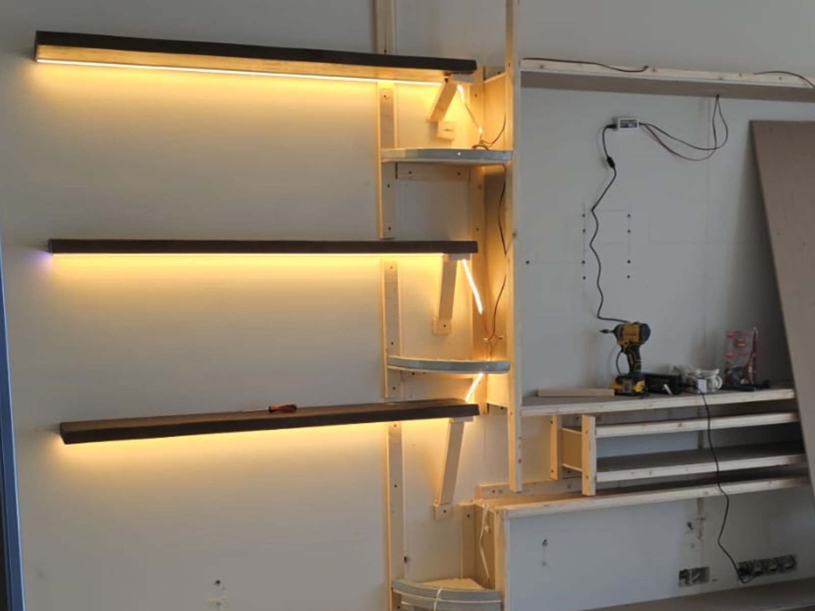 Verlichting in een cinewall: led-strips onder drie zwevende planken geven tijdens de bouw al een warme, indirecte gloed tegen de wand