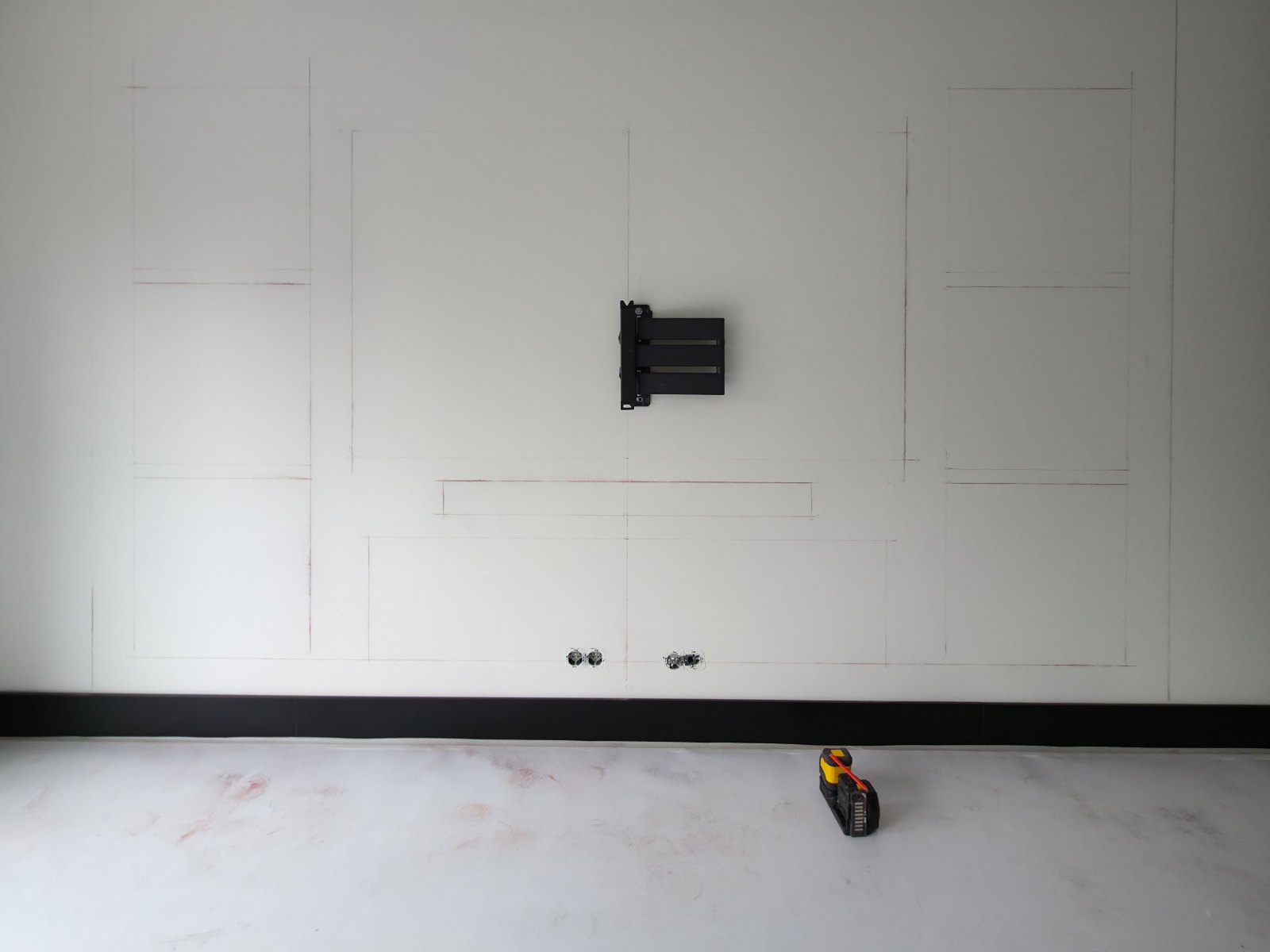 Cinewall zelf maken: de indeling met nissen en tv-vak in rood uitgetekend op de kale wand, met de muurbeugel en stopcontacten al gemonteerd