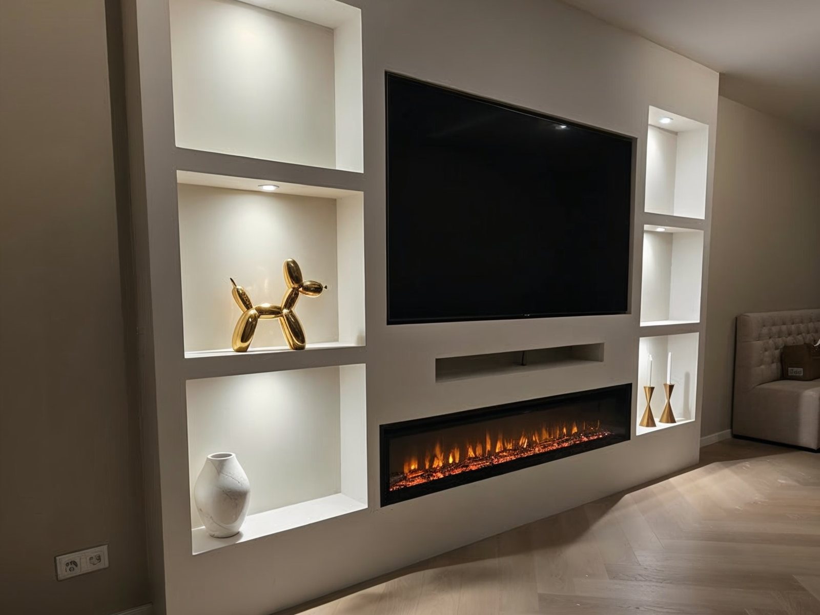 Tv wand idee in warme beige stijl: gestucte wand met zes verlichte nissen, verzonken tv, soundbar-nis en brede elektrische haard